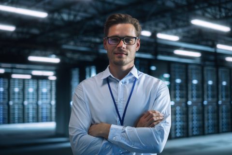 Male IT Engineer Working with Laptop in Data Center. Technician or Developer Standing at the Server Rack Corridor with a Laptop Computer. High-Speed Data Transfer, Analytics, Statistics Concept